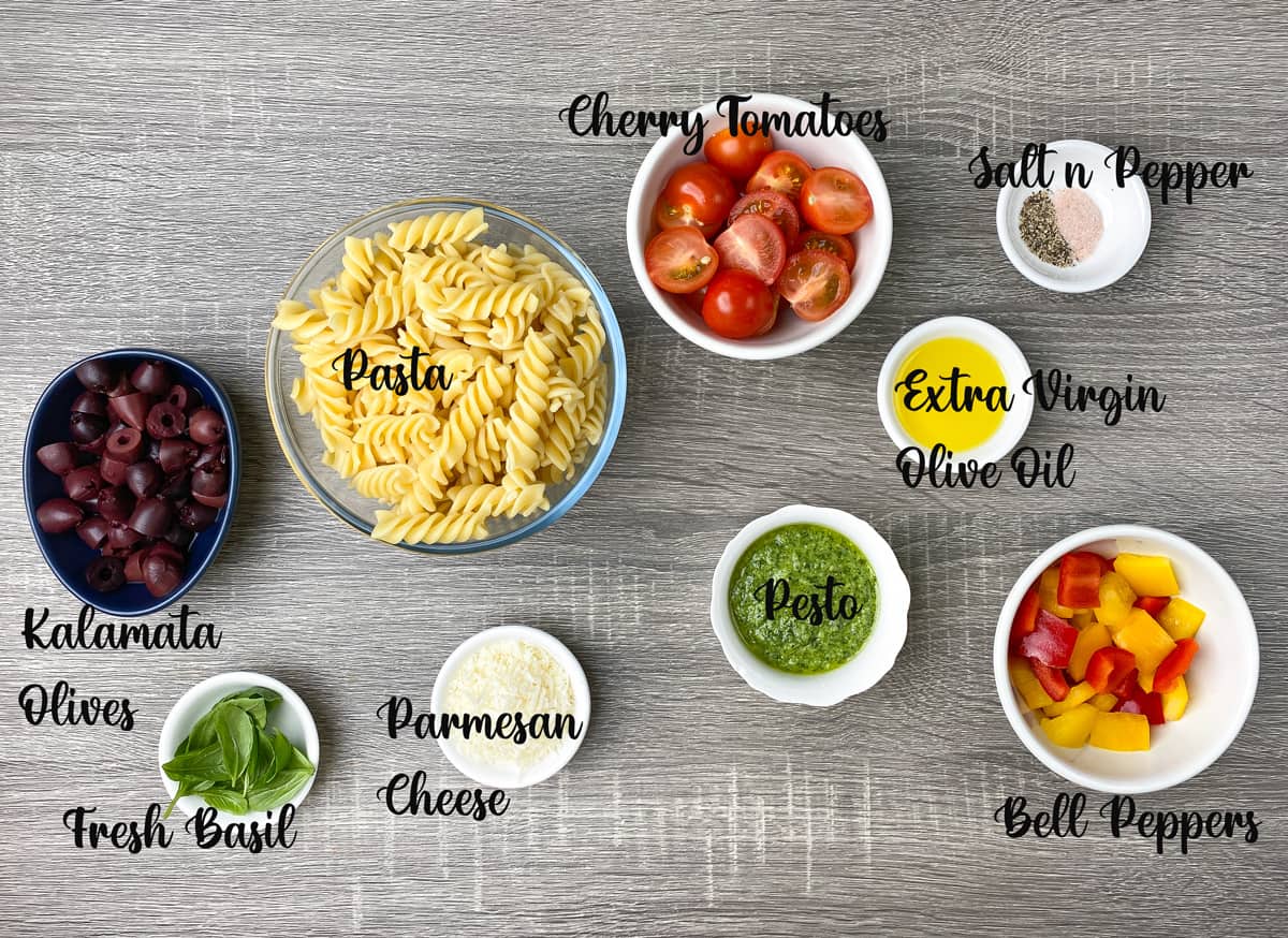 ingredients for making pesto pasta salad measured out in bowls on a wooden table