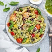 A serving bowl filled with pesto pasta salad and silver forks on a grey table