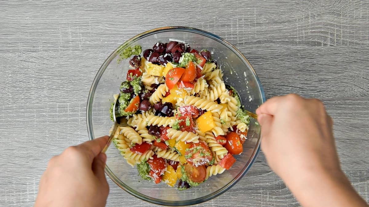 hands using spoons to toss the pasta salad