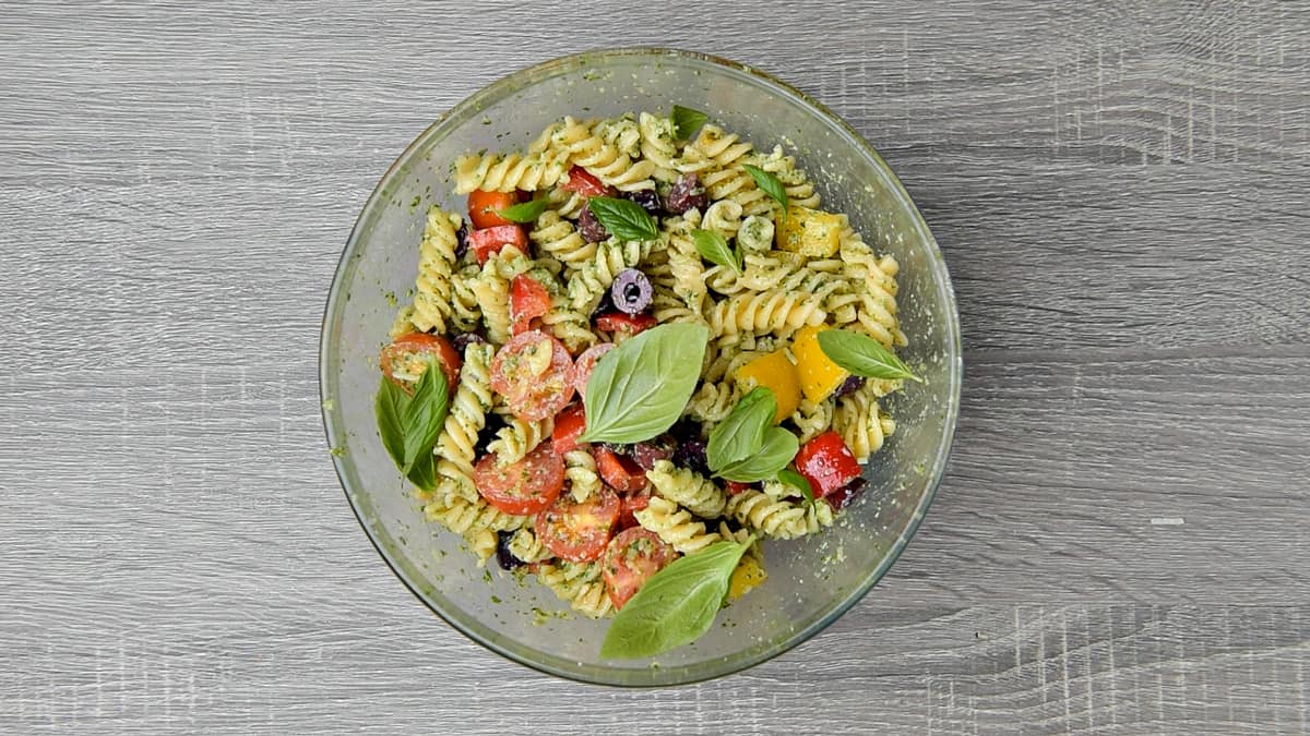 completed pesto pasta salad in a bowl garnished with fresh basil leaves