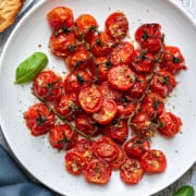 a pile of oven roasted cherry tomatoes on a white plate next to toasted bread slice
