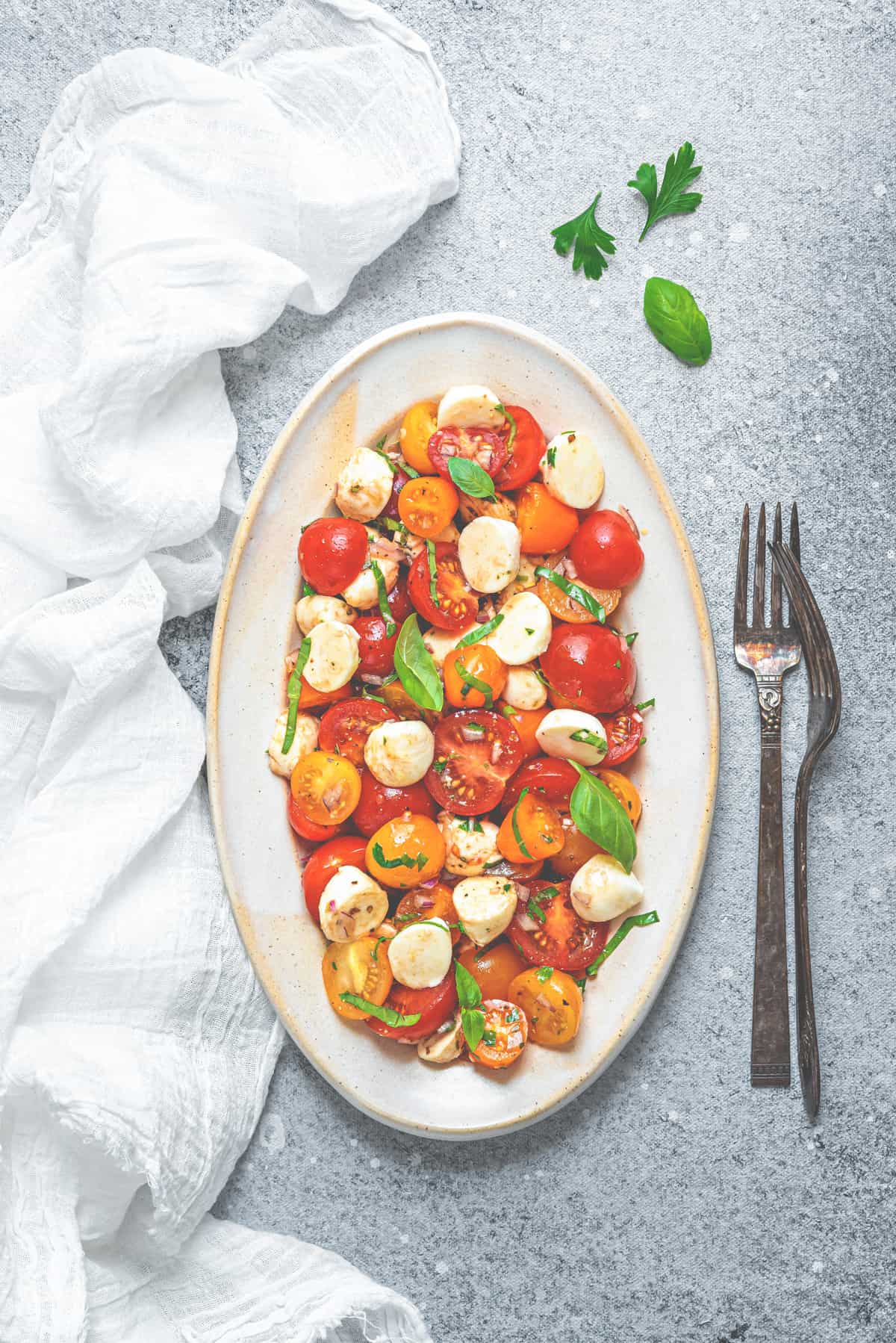 overhead shot of tomato and mozzarella salad on a large serving plate next to silver forks