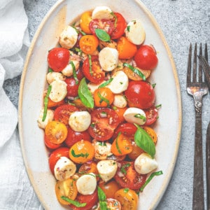 Oval serving plate filled with fresh tomato mozzarella salad and garnished with fresh basil