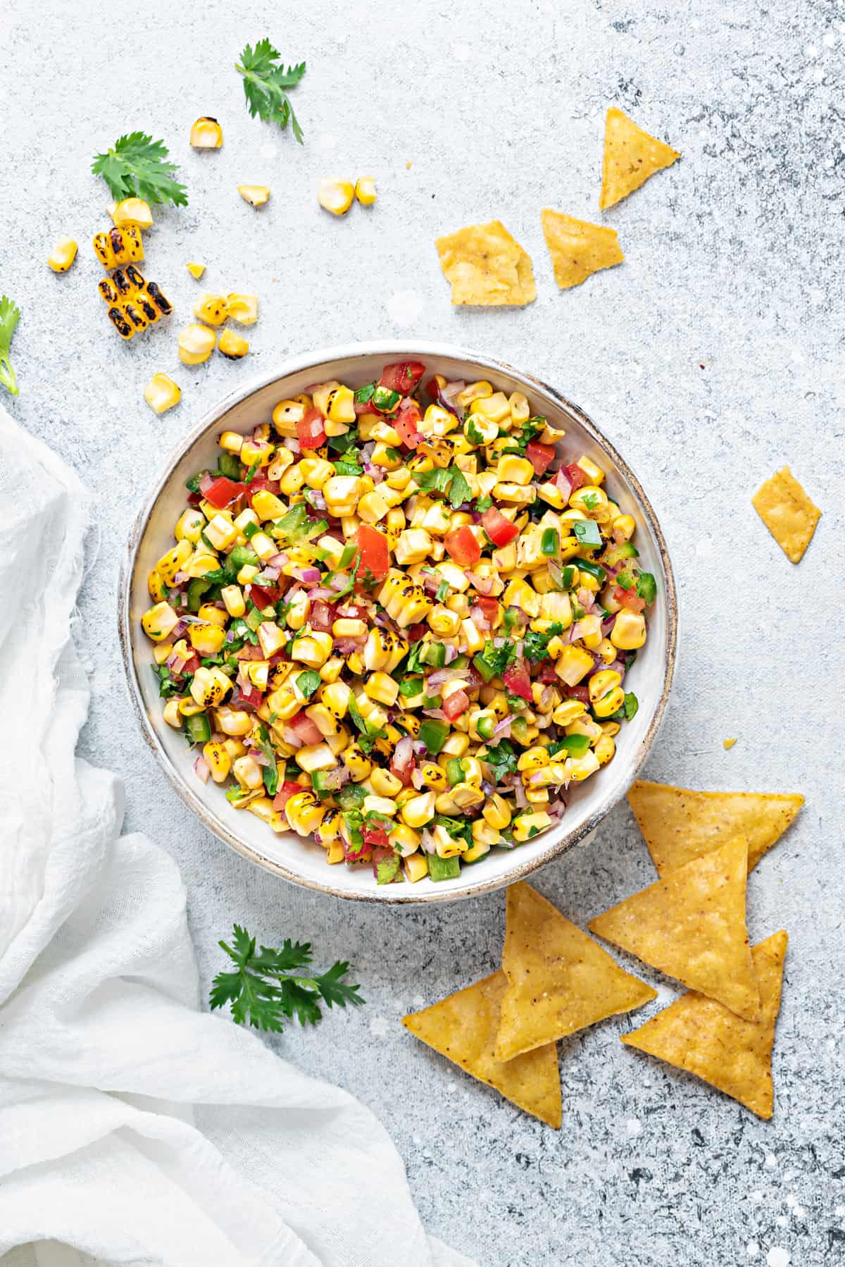 serving bowl of roasted corn and tomato salsa on a grey table with tortilla chips