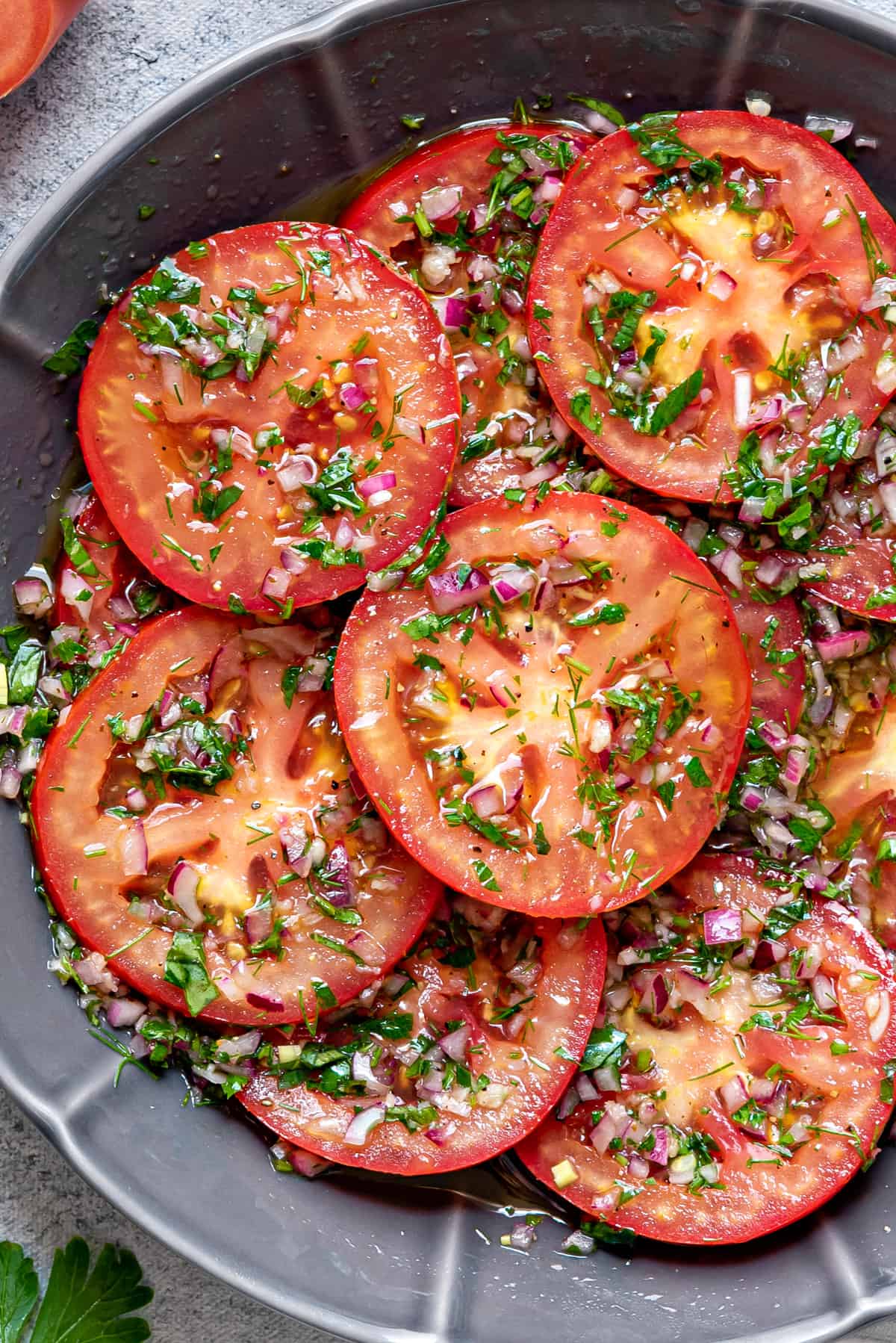 close up shot of vinaigrette and herbs marinated tomatoes salad in grey ceramic round plate