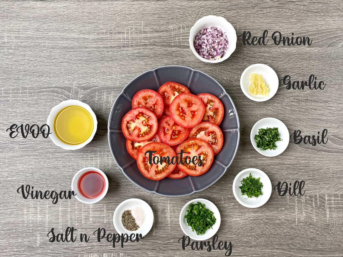 Ingredients for marinating the tomatoes placed in bowls and kept on grey table