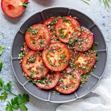 vinaigrette and herbs marinated tomatoes salad served in round grey ceramic plate