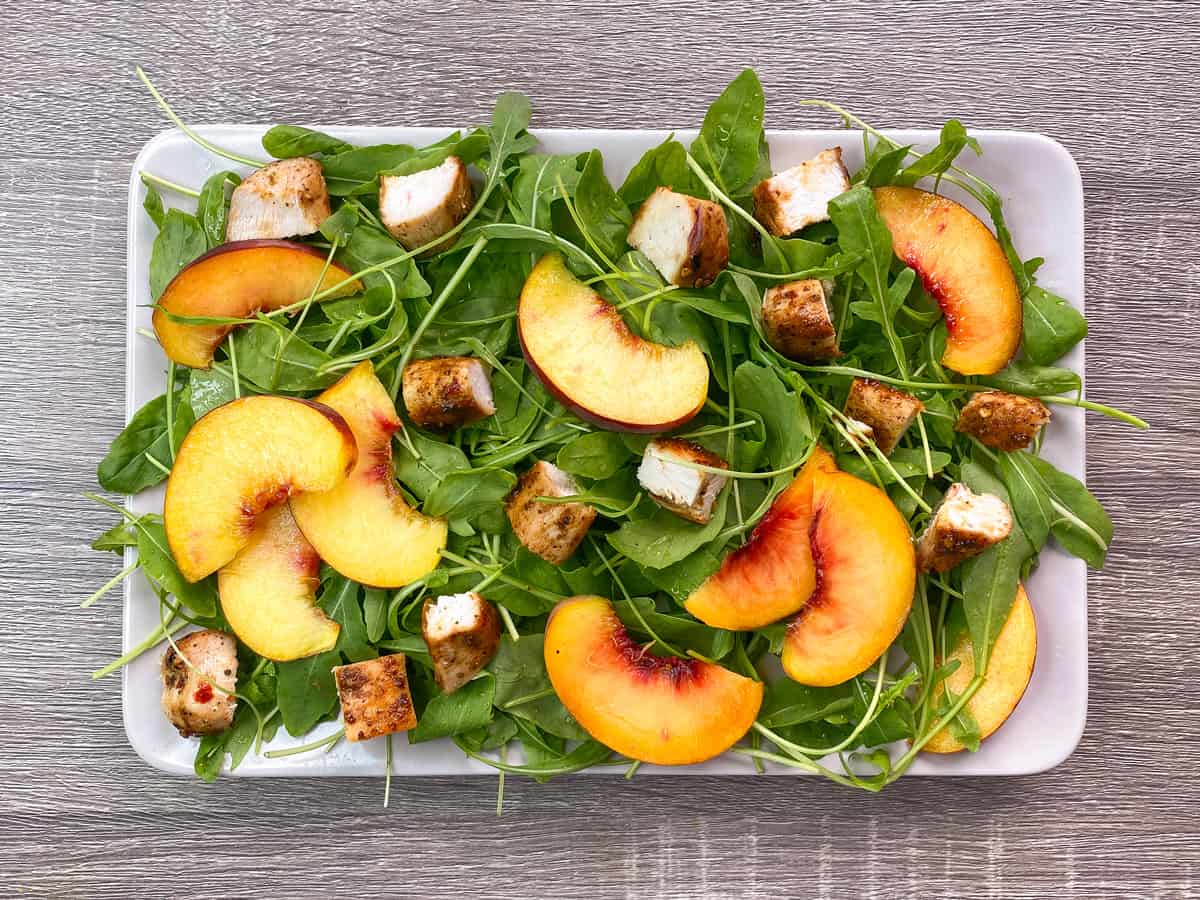 arugula, chicken and peaches artfully arranged on a rectangular serving platter