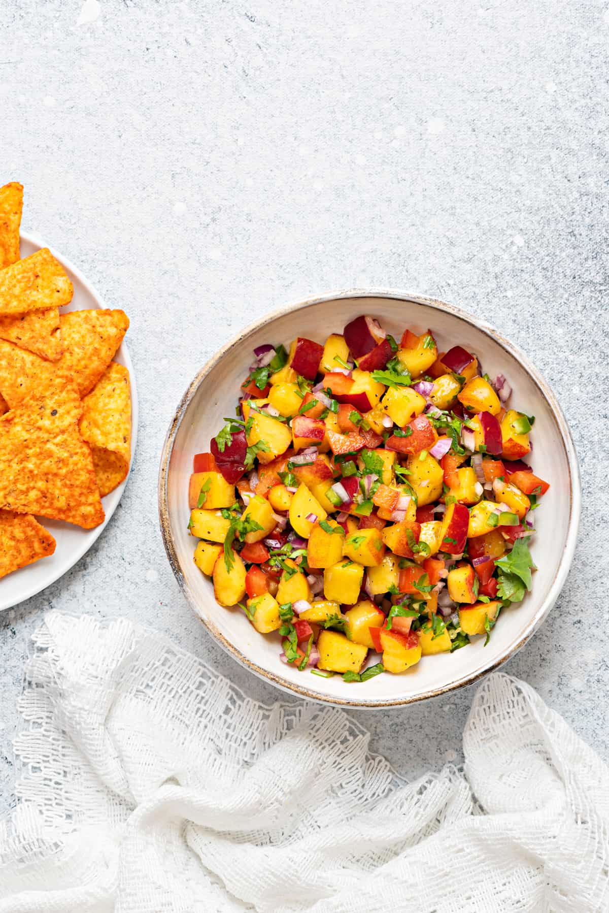 peach salsa in a white serving bowl with tortilla chips in a plate on the side 