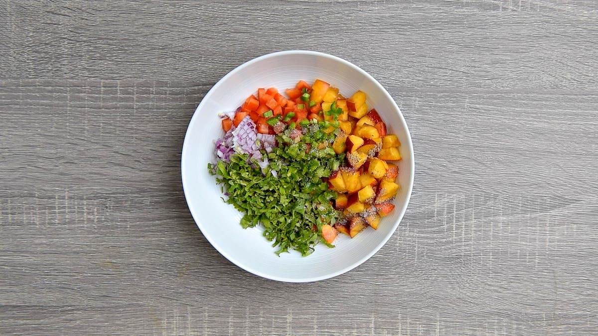 all ingredients for making peach salsa added to a mixing bowl