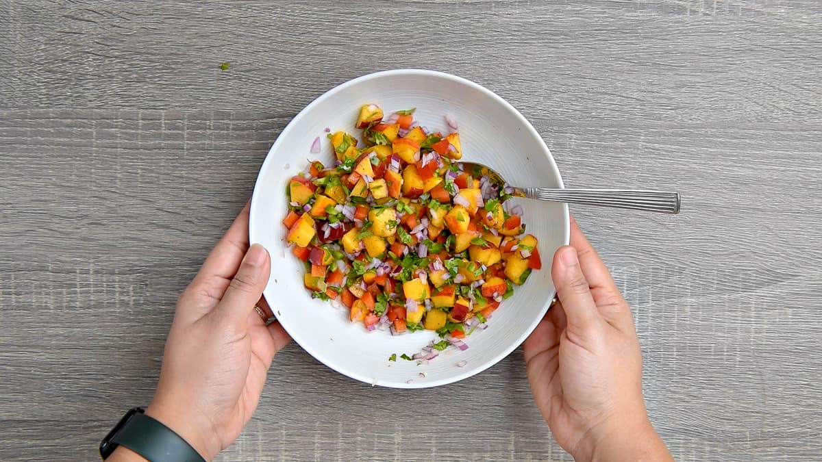 hands holding mixing bowl after stirring salsa ingredients together