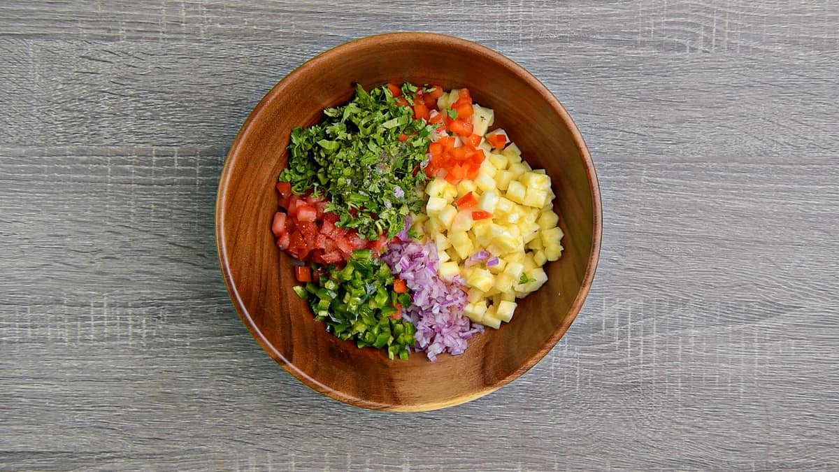 all pineapple salsa ingredients added to wooden salad bowl