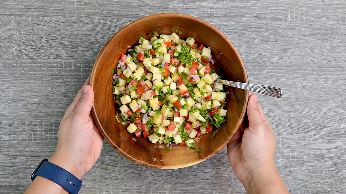 hands holding wooden mixing bowl after stirring pineapple salsa together