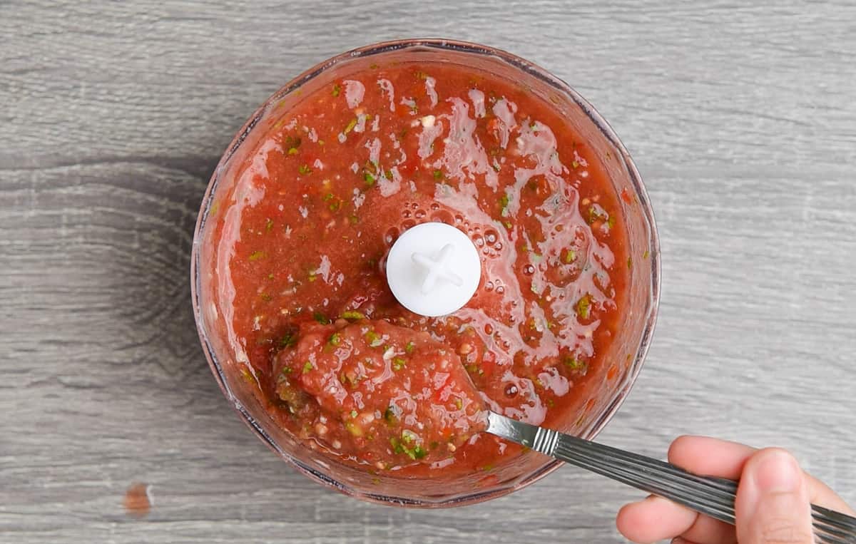 taking a spoonful of homemade fresh and spicy salsa from the food processor