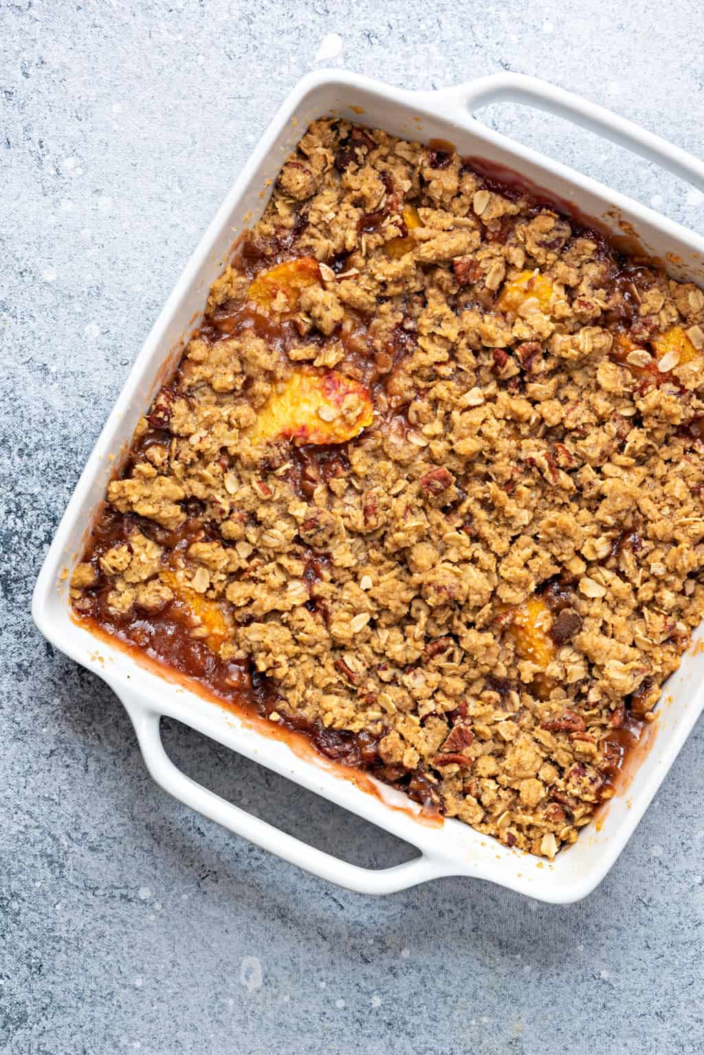 warm peach crisp with oat topping in a white baking dish on a grey table
