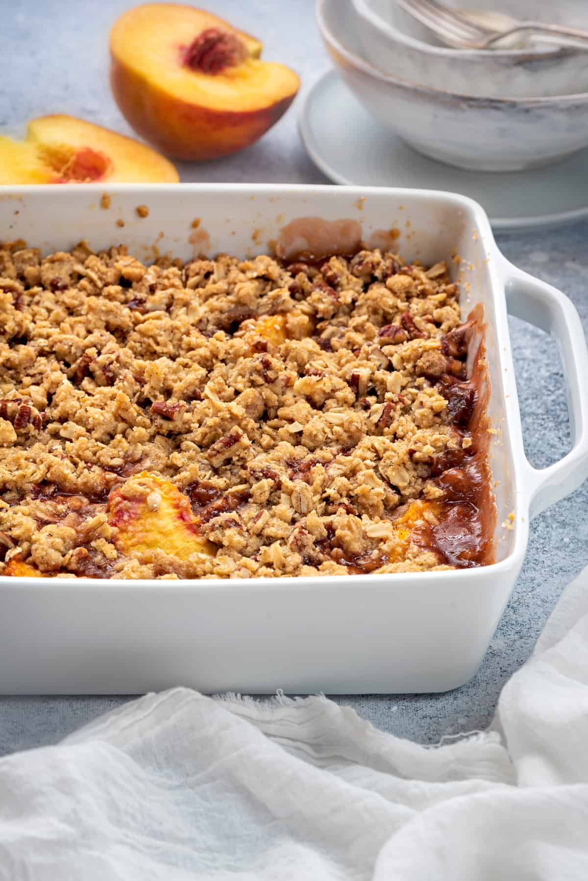 healthy peach crisp with oat topping in a white casserole dish on a grey table