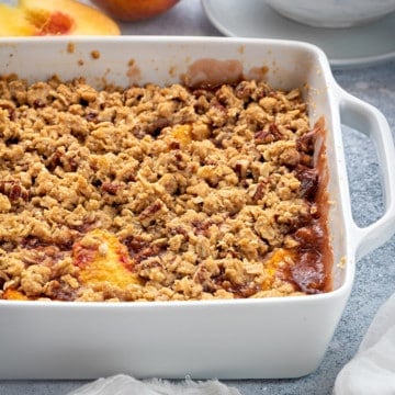 healthy peach crisp with oat topping in a white casserole dish on a grey table