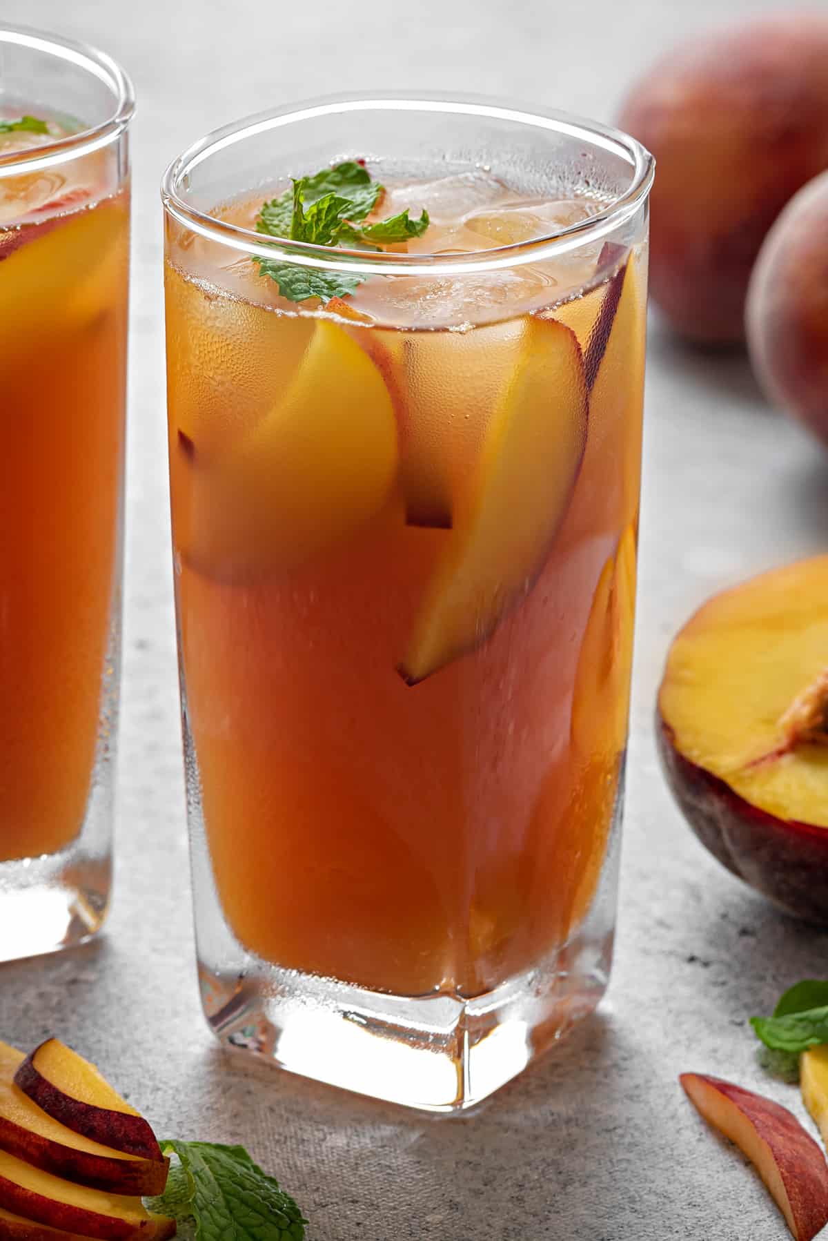 a tall glass with refreshing peach iced tea, peach slices and some fresh mint