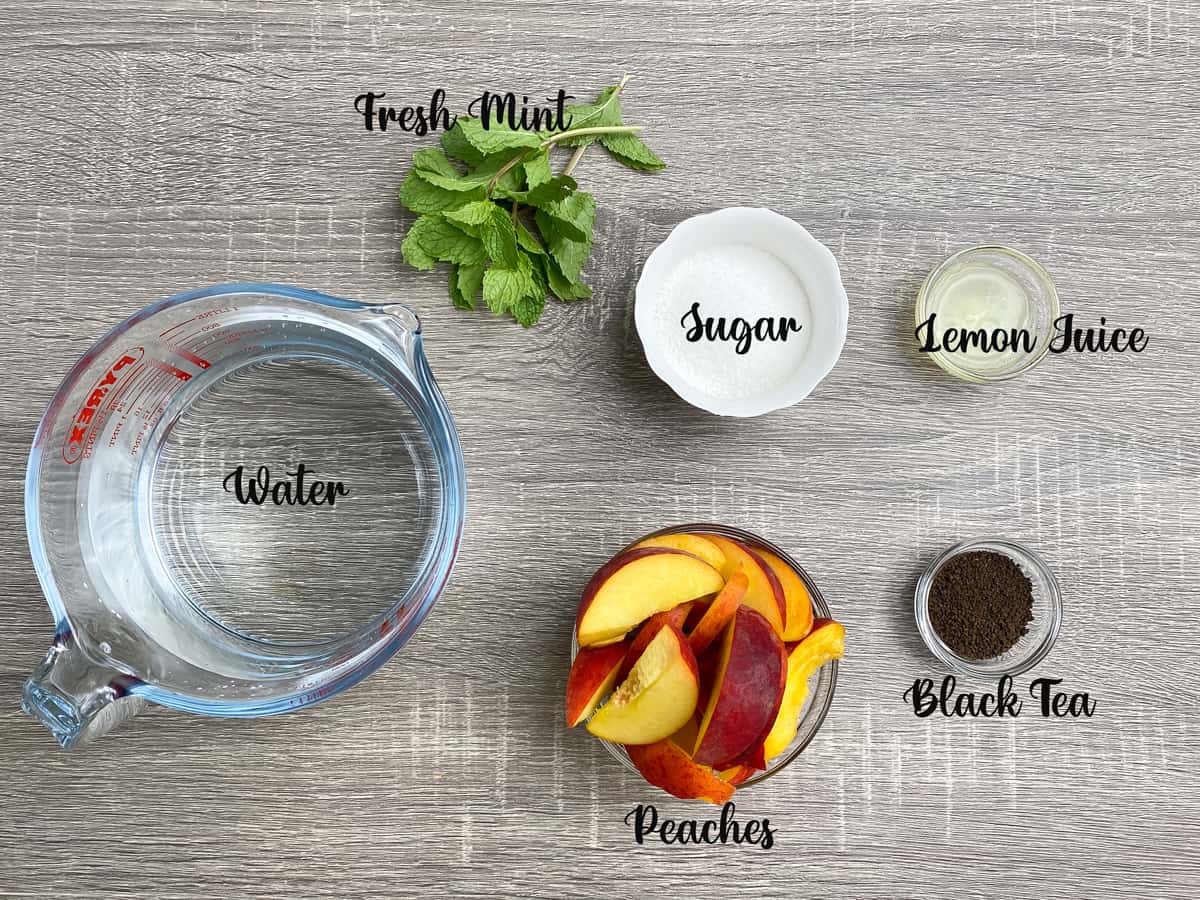 ingredients for peach iced tea measured in bowls and a jar on a grey table