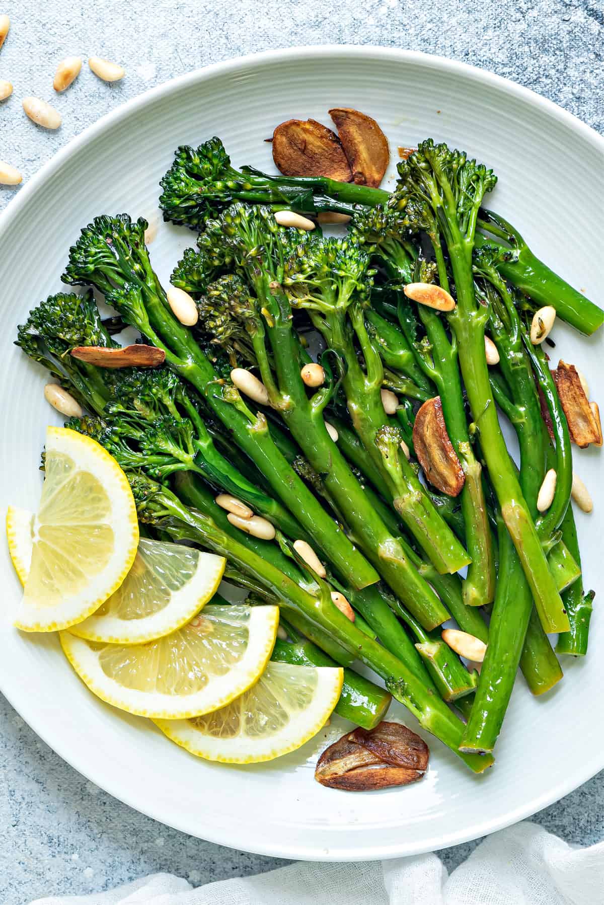 a round white plate of sautéed broccolini finished with garlic chips, pine nuts and lemon 