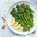 a round white plate of sautéed broccolini finished with garlic chips, toasted pine nuts and lemon