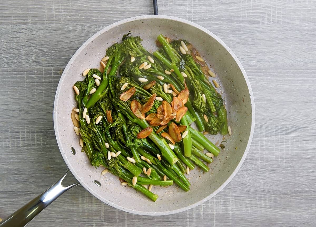 broccolini is cooked to al dente from pan frying and steaming, then finished with lemon juice, garlic chips and pignolias