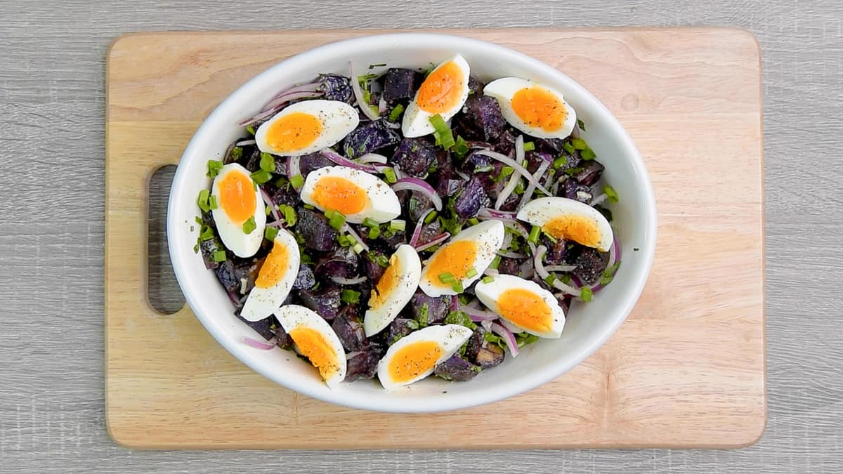 tossed purple potato salad in a serving bowl topped with wedges of jammy eggs