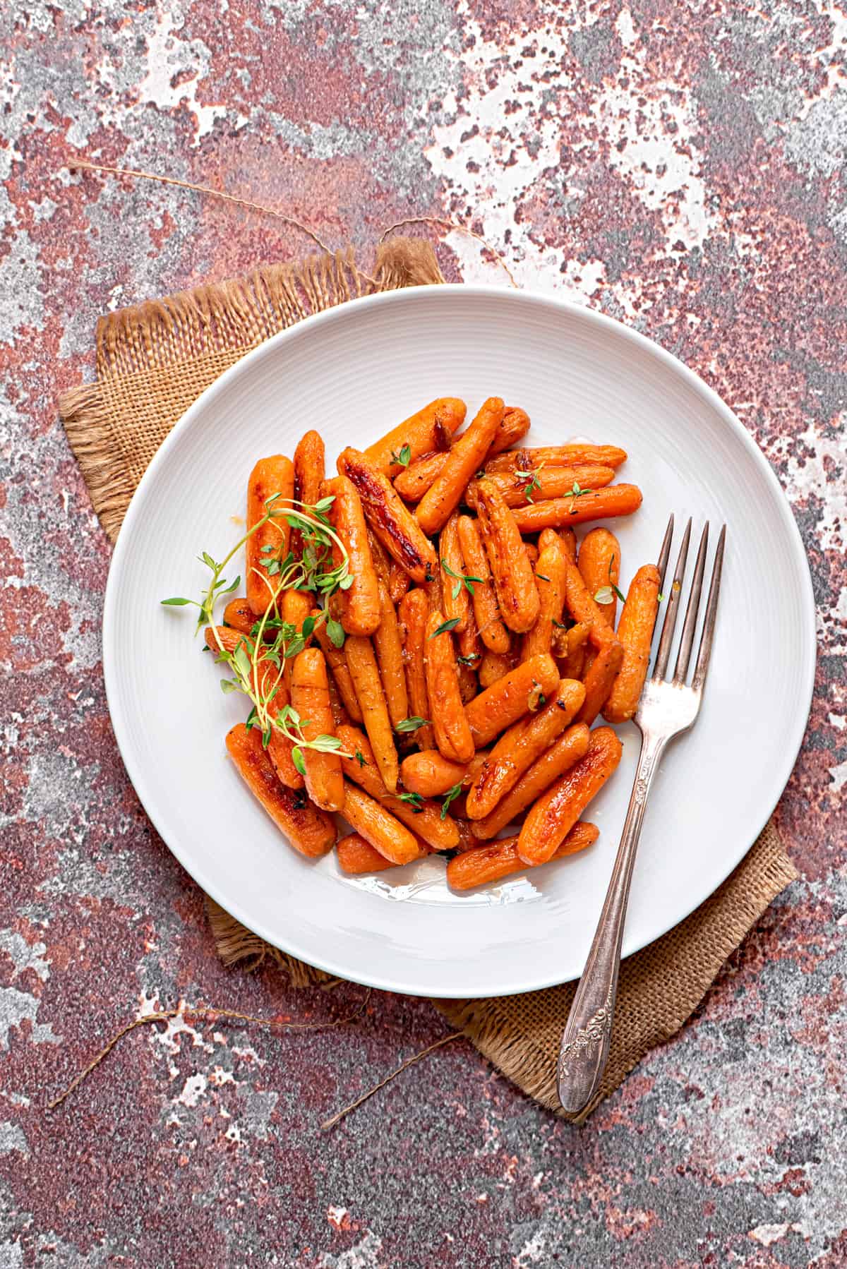 white dinner plate filled with maple roasted baby carrots and a silver fork