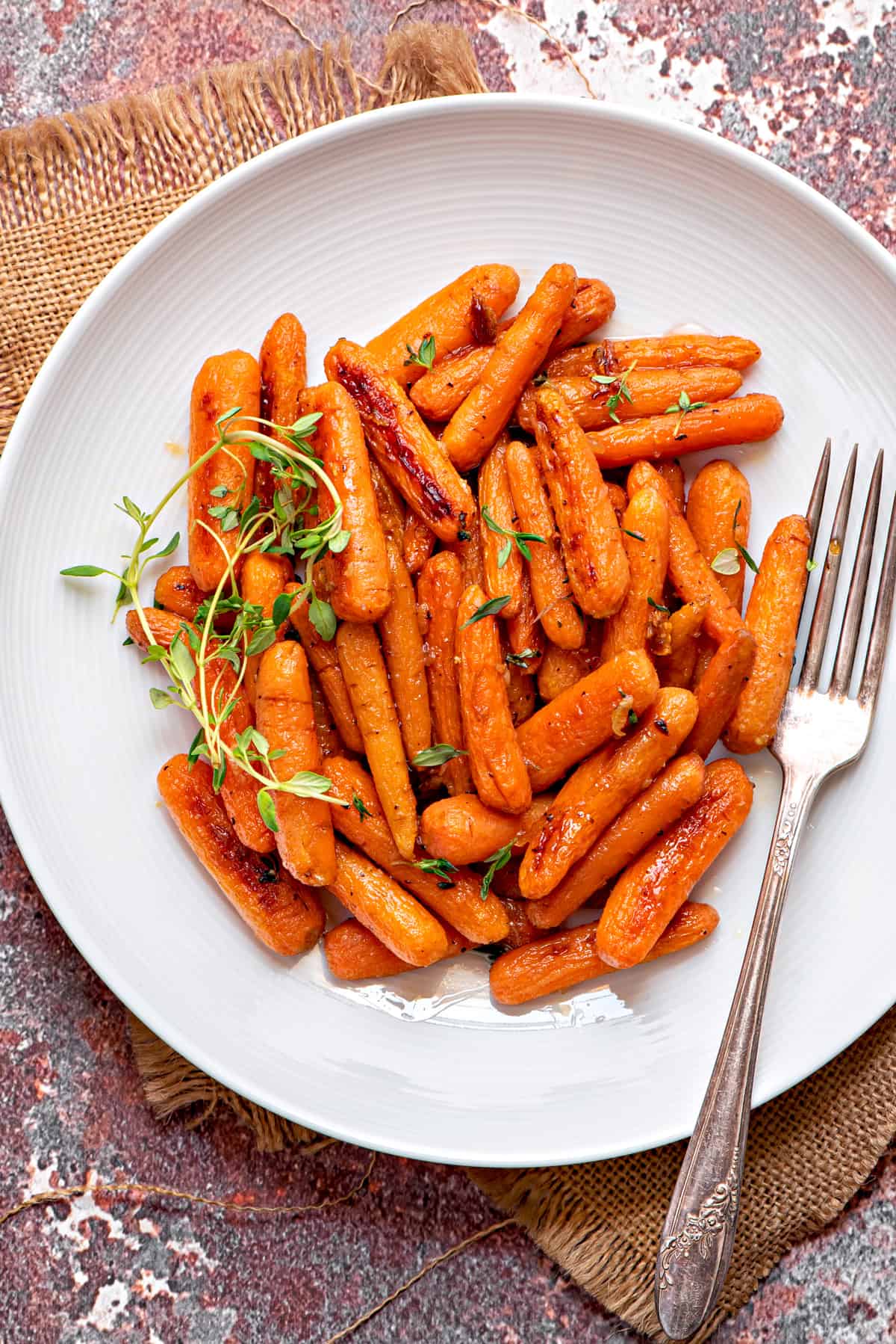 overhead shot of white dinner plate filled with maple thyme roasted baby carrots and a silver fork