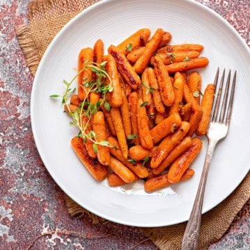 white dinner plate filled with maple thyme roasted baby carrots and a silver fork