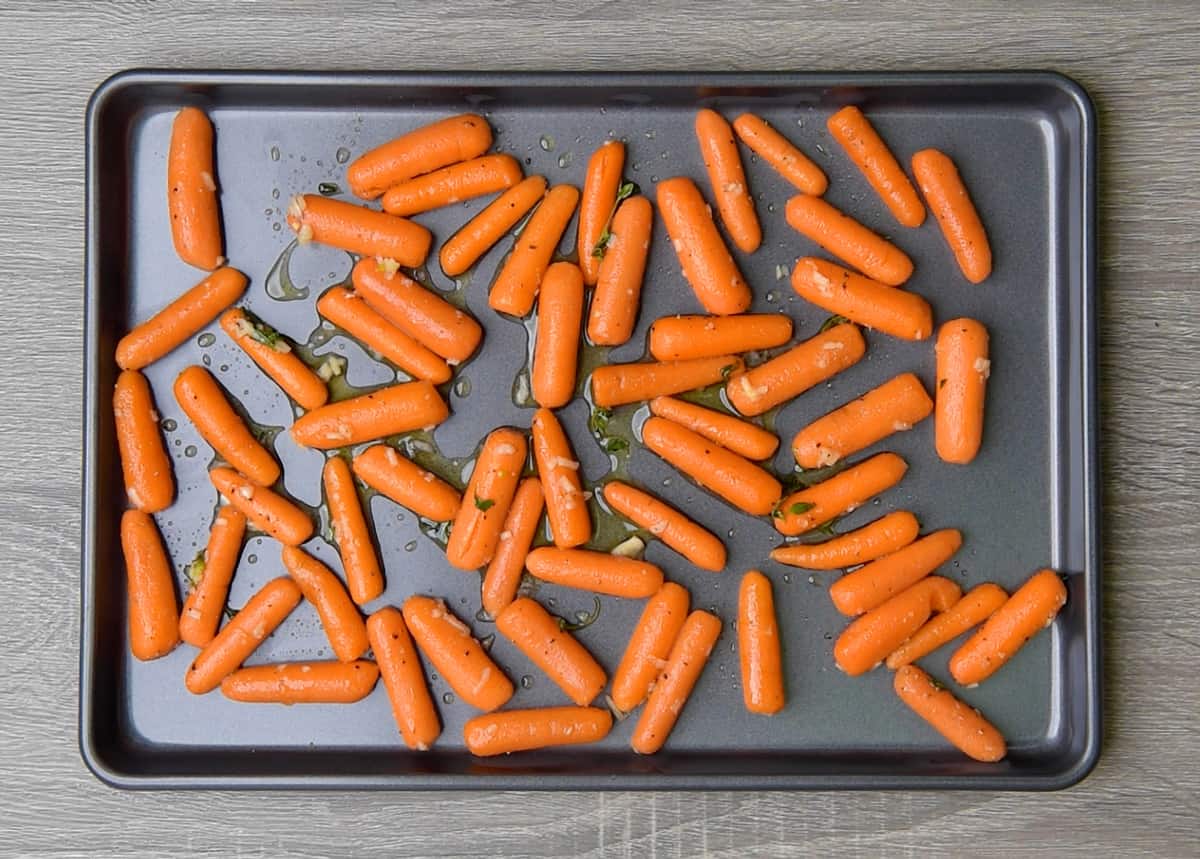 baby carrots on a sheet pan after tossing with oil, maple syrup, garlic and thyme