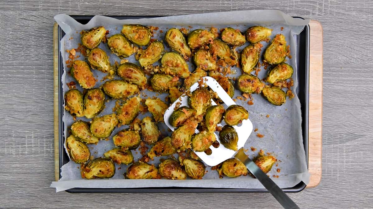 spatula removing golden brown roasted brussel sprouts from sheet pan