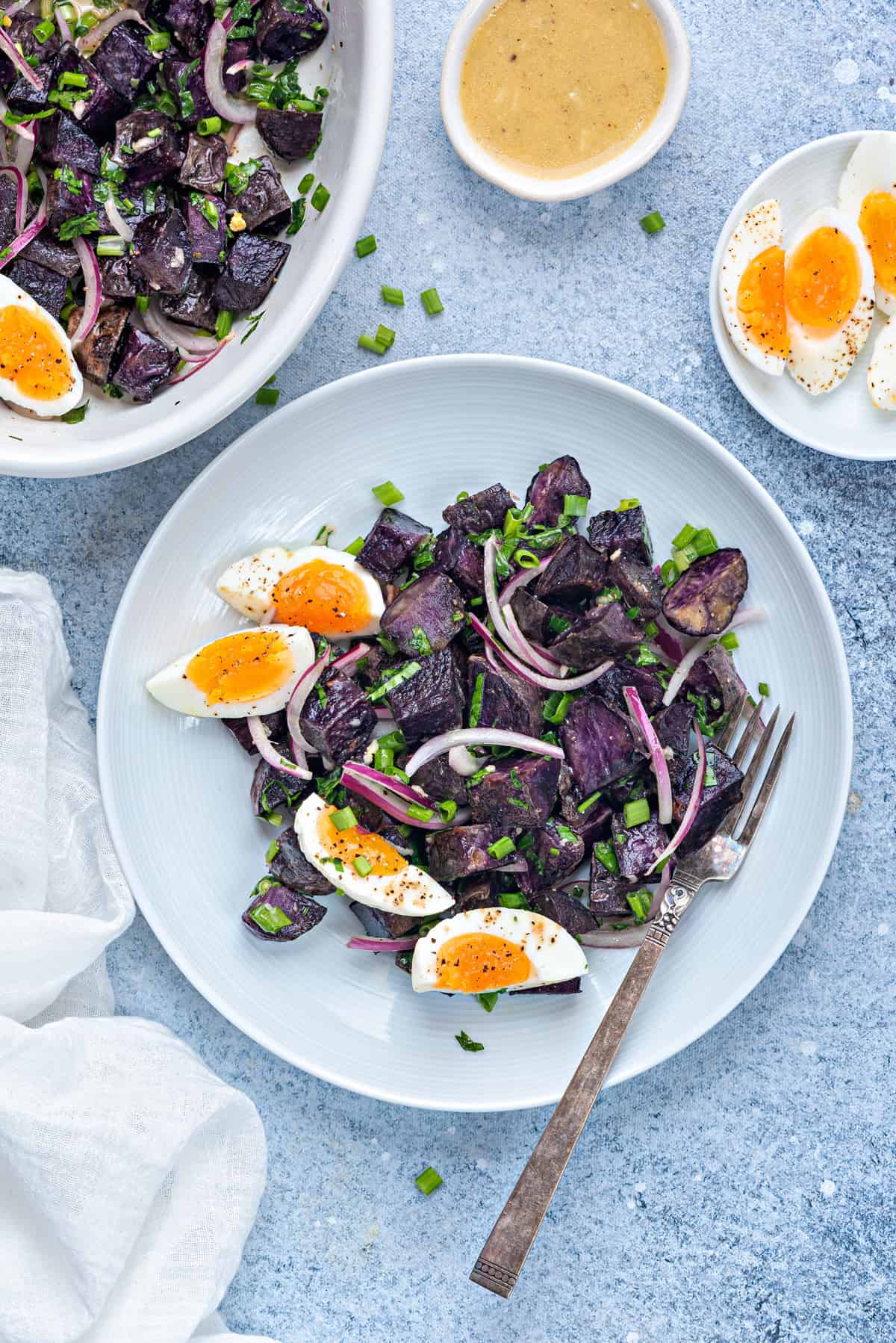 warm purple potato salad in a white plate with 7 minutes egg wedges and a silver fork