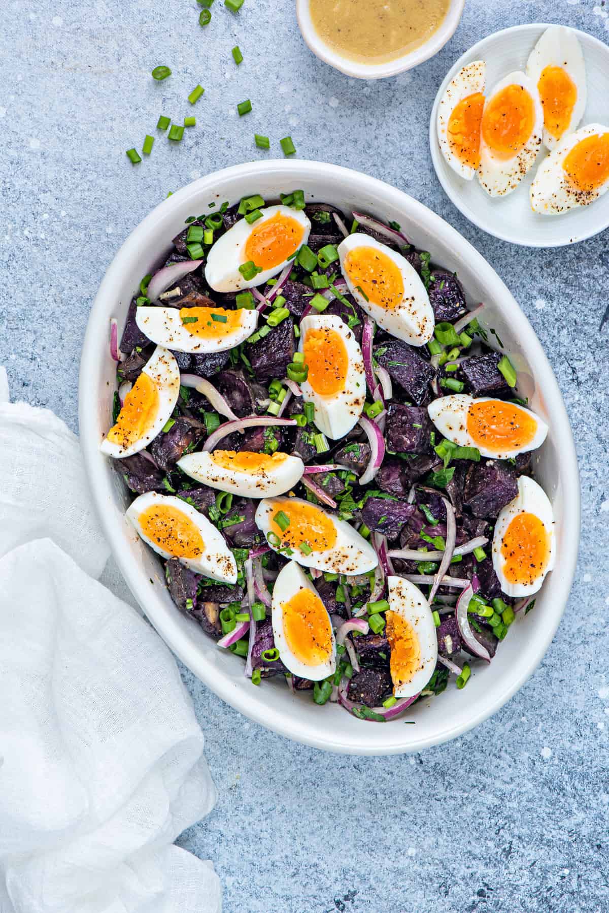 warm purple potato salad in white serving dish with a garnish of soft boiled eggs