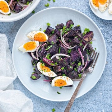 warm purple potato salad in a white plate with 7 minutes egg wedges and a silver fork