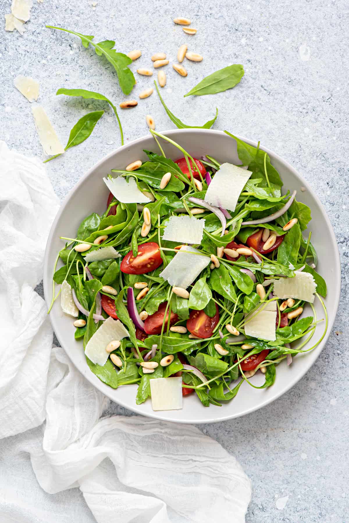 one bowl of arugula salad with pine nuts, parmesan, tomatoes, onions 