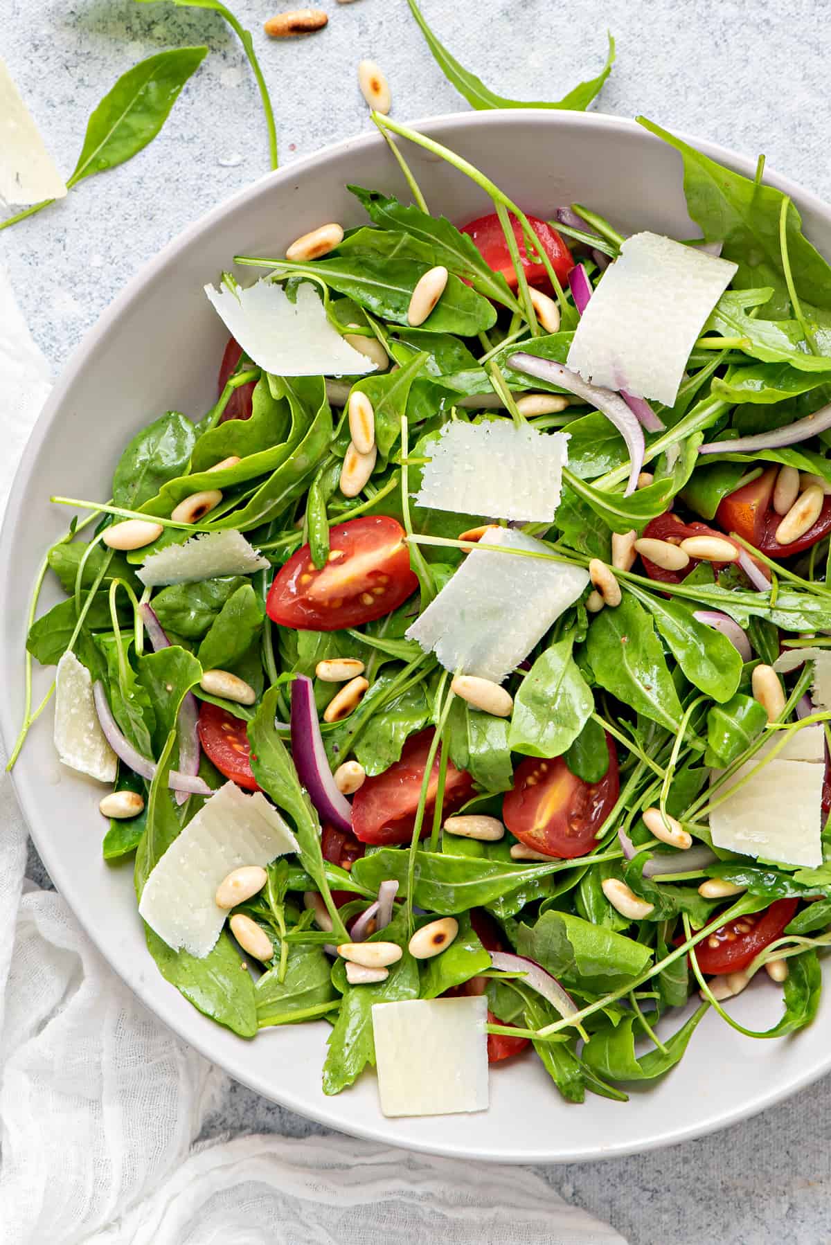 white bowl of simple arugula salad with onions, tomatoes, pinenuts, and parmesan