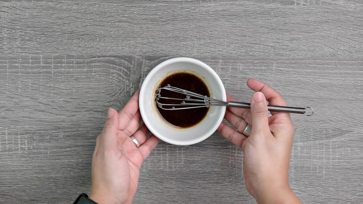 hands holding a small bowl with balsamic lemon vinaigrette and a whisk 