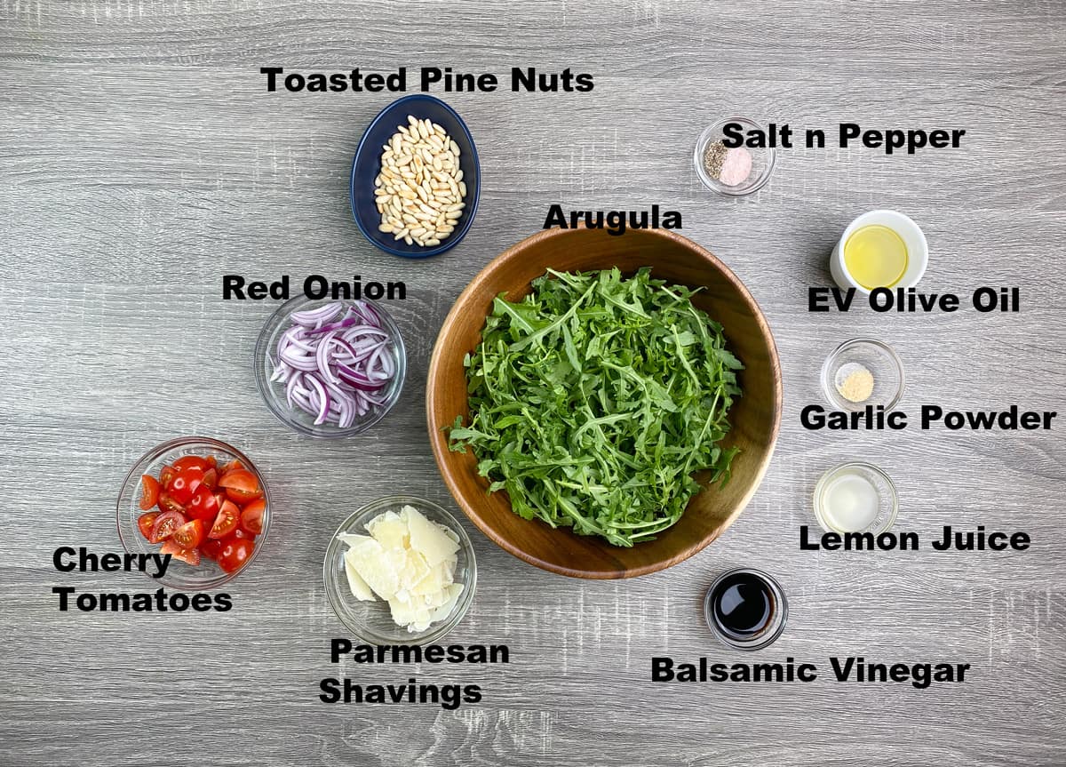 ingredients for arugula salad and dressing measured in bowls and placed on grey table