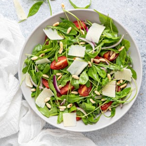 white bowl filled with arugula, tomatoes, onions, pine nuts, and parmesan
