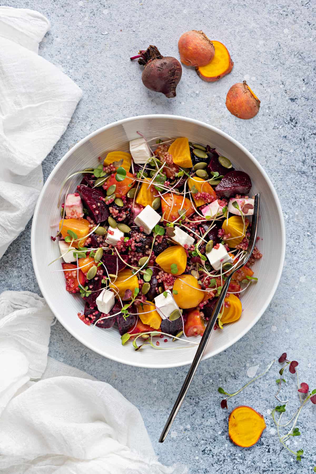 beetroot salad with feta, quinoa, microgreens in white bowl with fork