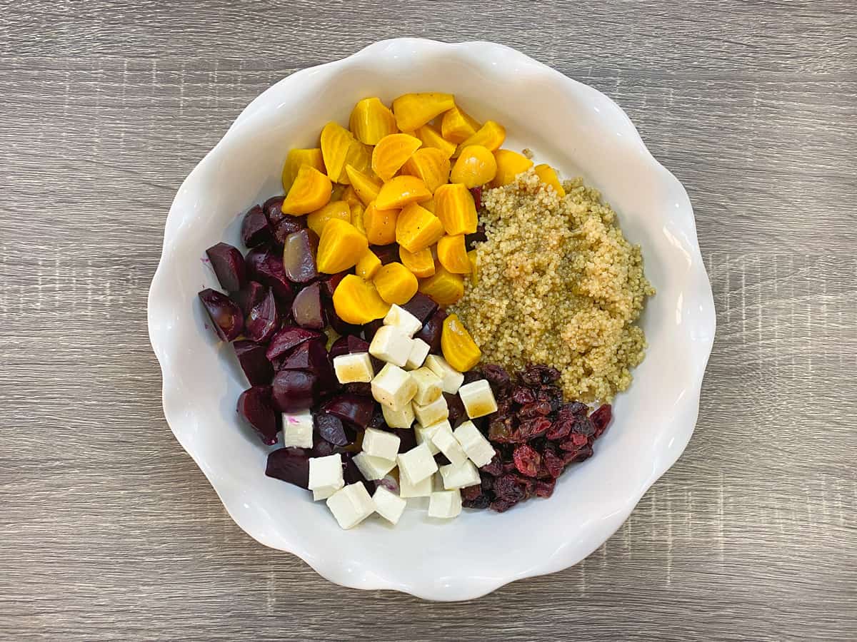 cooked red and golden beets in white bowl with quinoa, feta, and cranberries