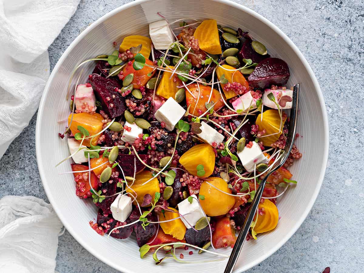 beet salad with feta in white bowl with microgreens and cranberries