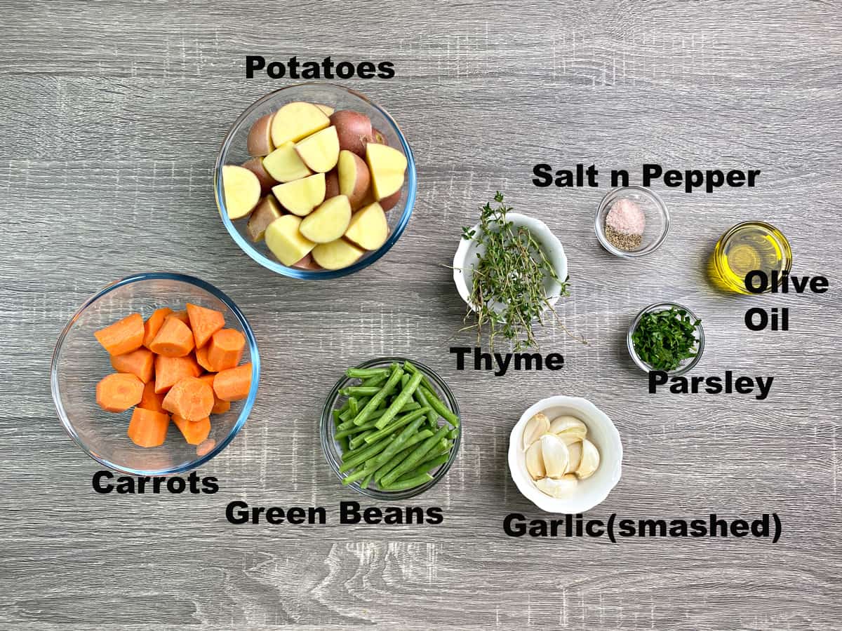 diced potatoes, carrots, trimmed green beans, fresh herbs, garlic, salt, pepper, and olive oil in different bowls 