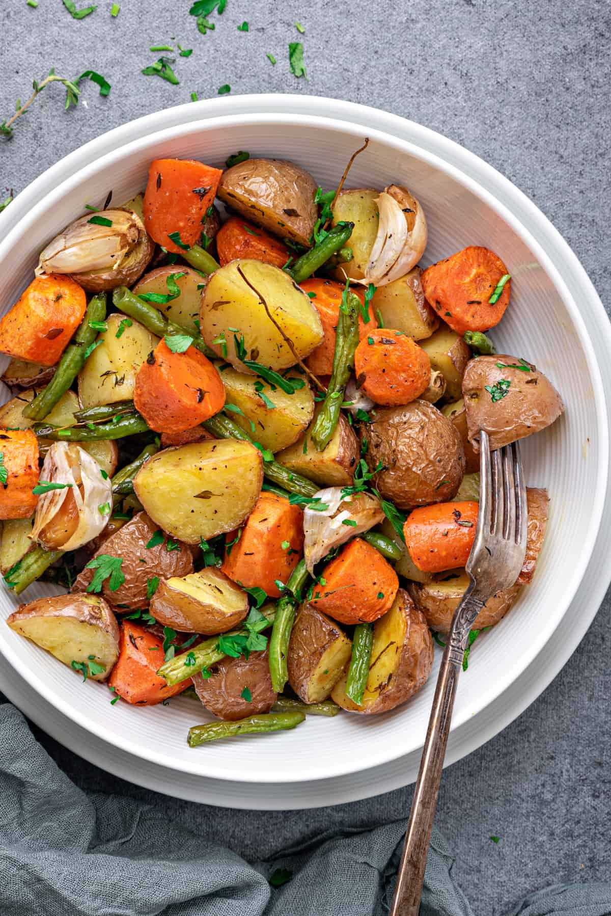 top view of roasted potatoes, carrots and green beans with herbs in white bowl with fork 