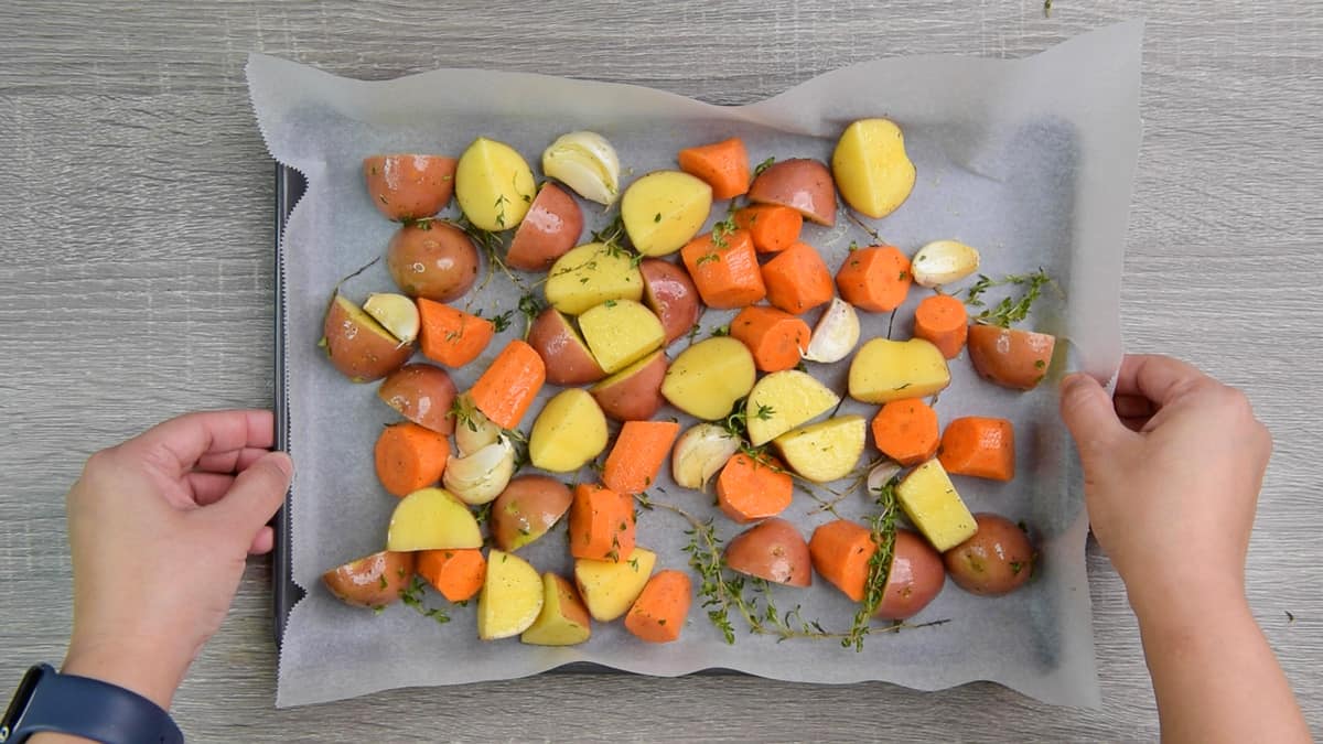 oiled and seasoned carrots and potatoes on baking sheet with parchment paper 