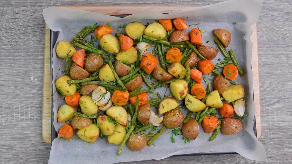 roasted carrots, potatoes, green beans, and herbs on baking dish with parchment paper