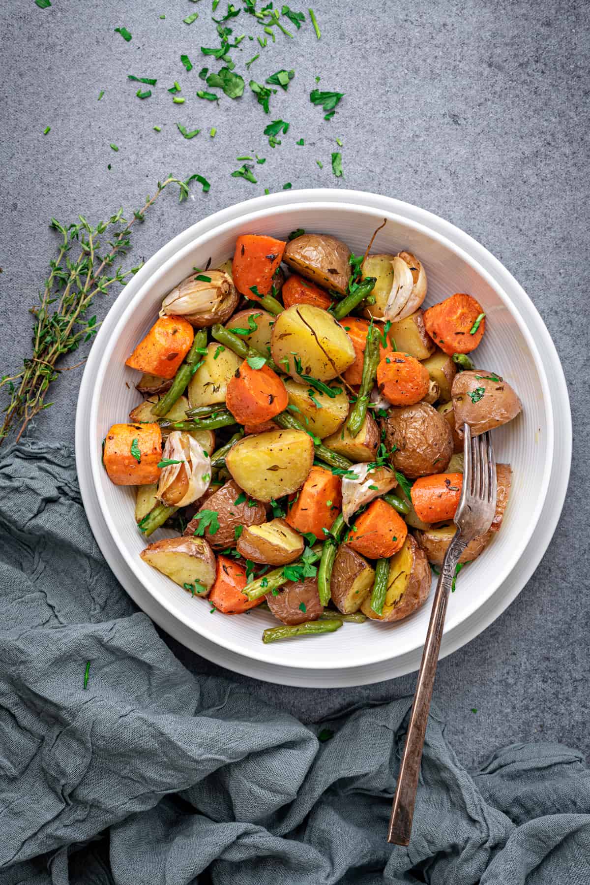 roasted potatoes, carrots, green beans, and thyme on white plate with fresh herbs 