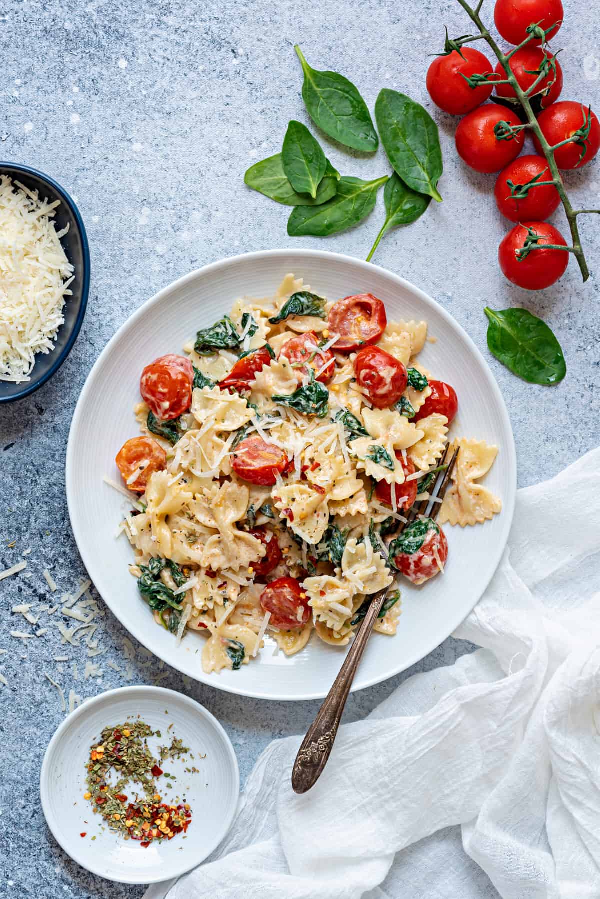 pasta with spinach and tomatoes on white plate with parmesan cheese 