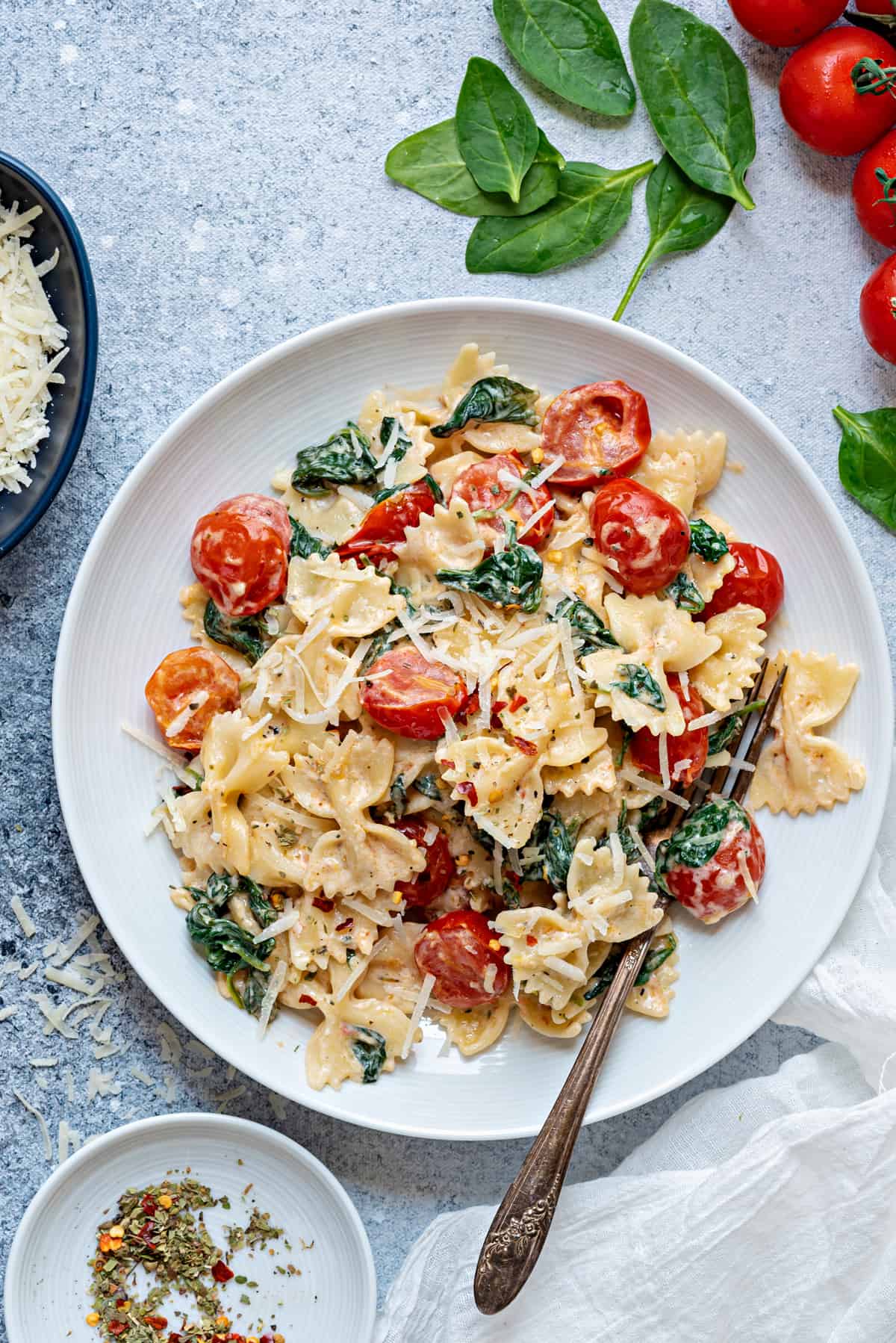 one white plate filled with tomato spinach pasta and topped with parmesan